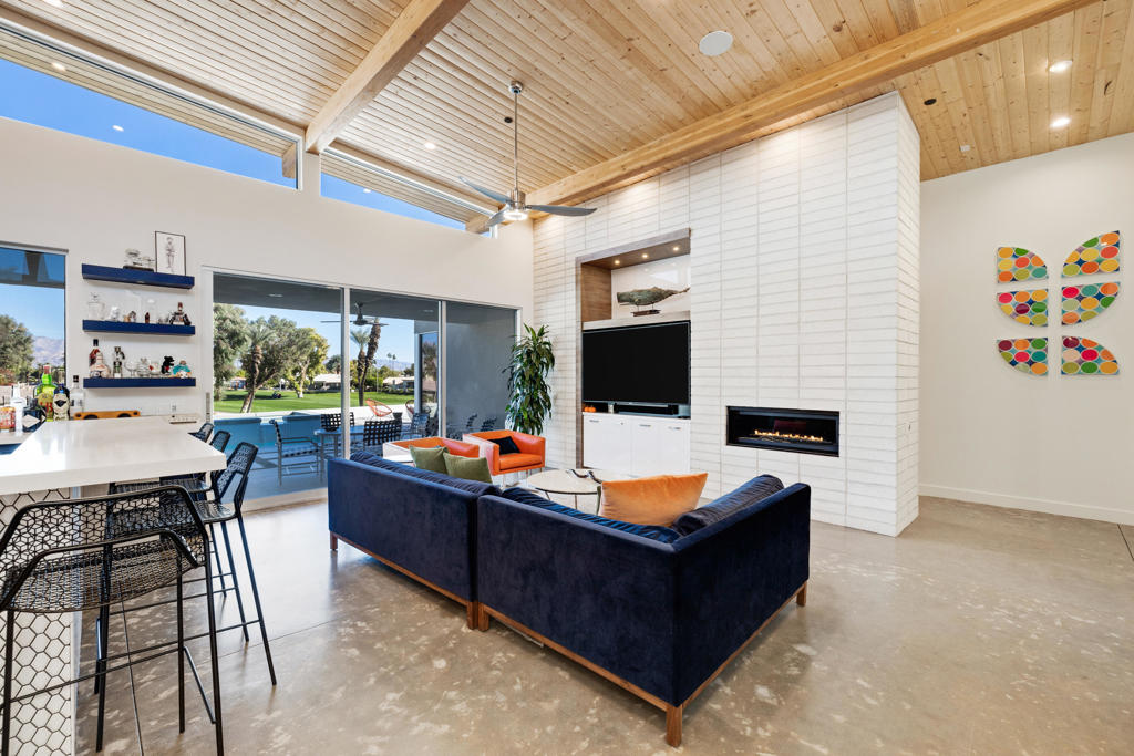 Open-plan living room with a vaulted wood ceiling, navy sectional, linear fireplace, and wide patio doors.