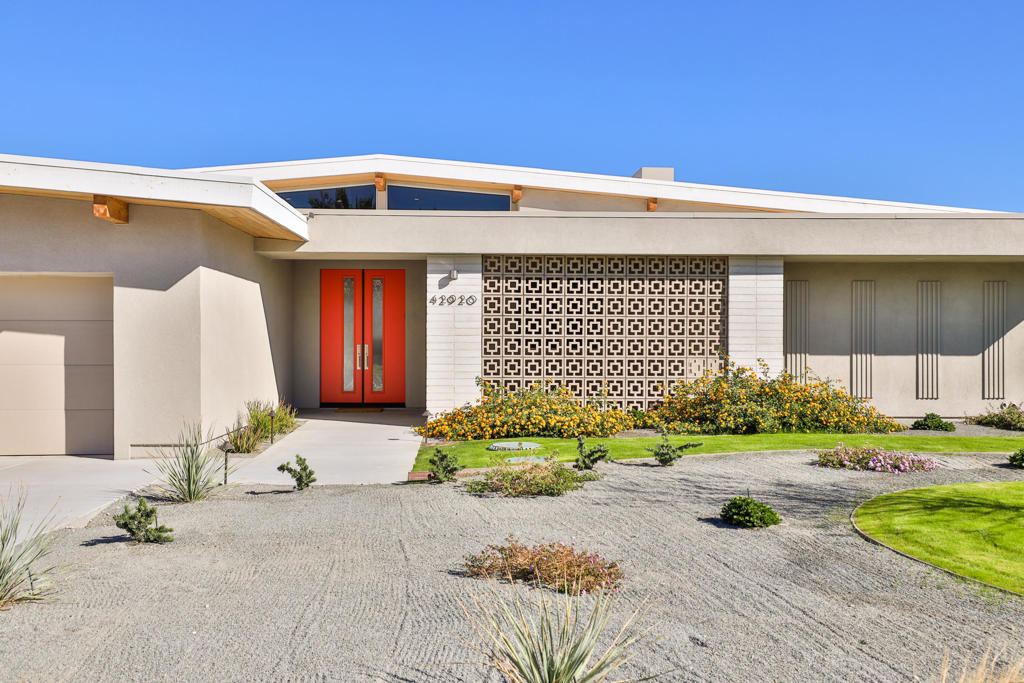 Modern home exterior with red double doors, geometric screen, and gravel desert landscaping.