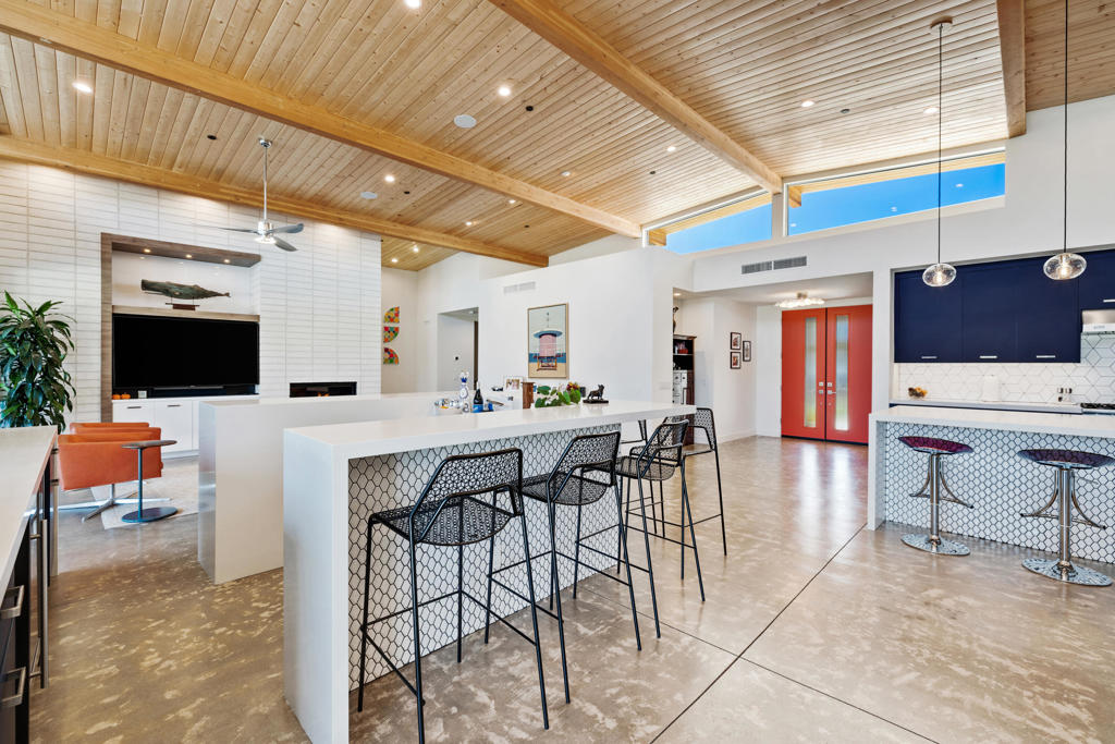 Open-plan kitchen with a long island, navy cabinets, and a vaulted wood ceiling.