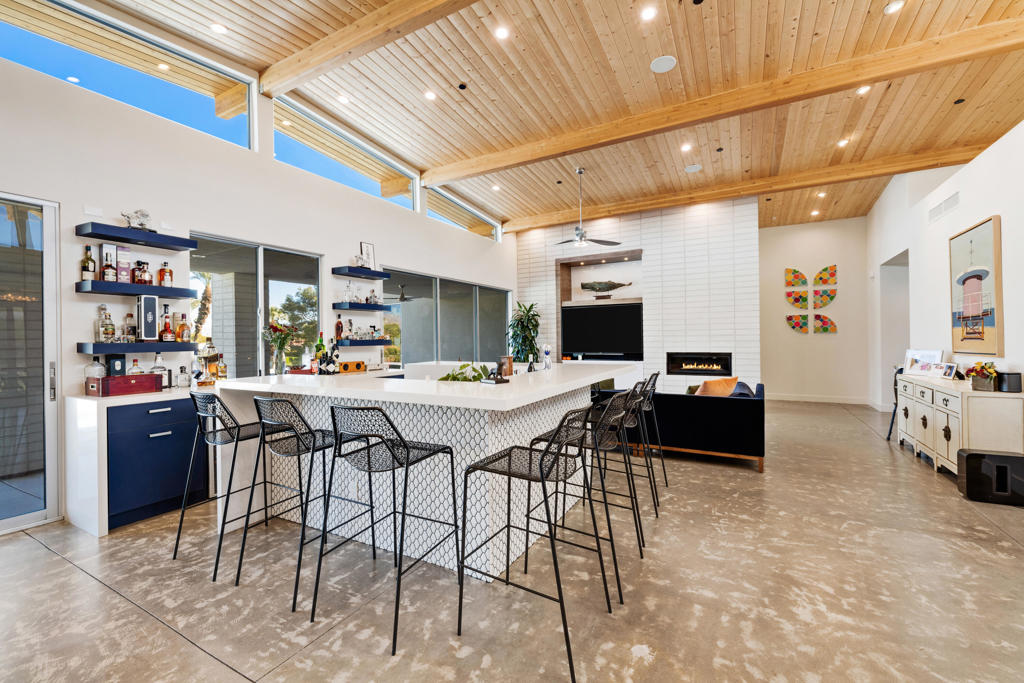 Open-plan kitchen with a large white island, bar stools, and a vaulted wood-plank ceiling.