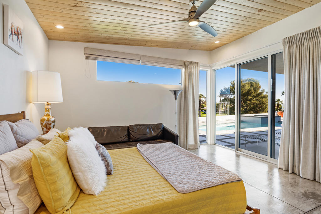 Bedroom with a yellow quilted bed and sliding glass doors overlooking the pool.