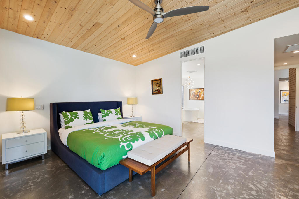 Bedroom with green patterned bedding, a wood plank ceiling, and polished concrete floors.