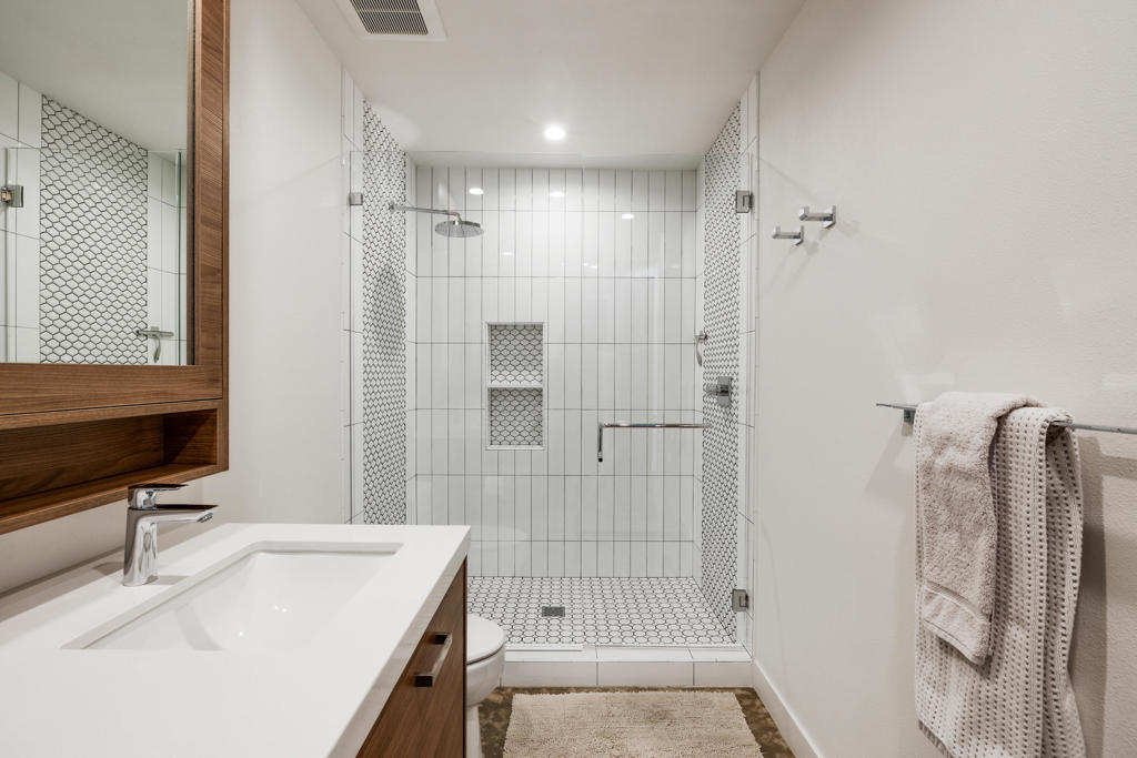 Bathroom with a glass-enclosed tiled shower and wood vanity with white sink.