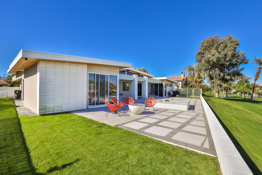 Modern single-story home with a paved patio, orange chairs, and manicured lawn.