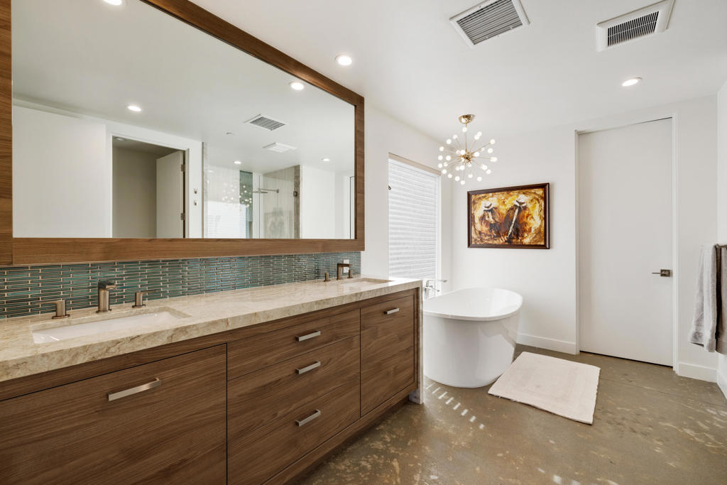 Bathroom with a long wood double vanity, teal tile backsplash, and freestanding soaking tub.