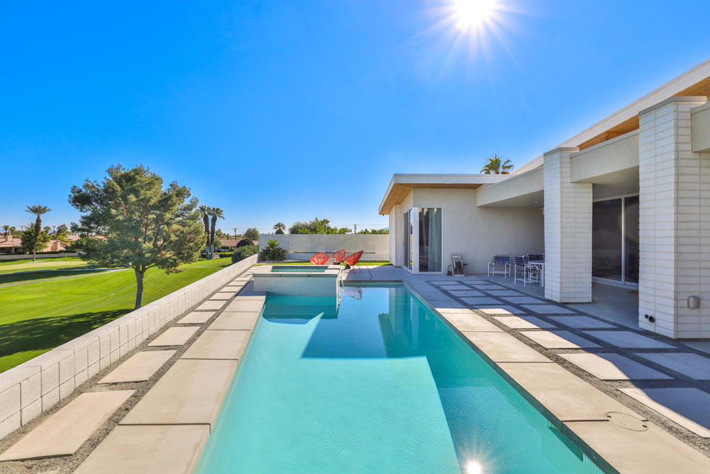 Modern home beside a long pool, with geometric patio pavers and a golf course view.