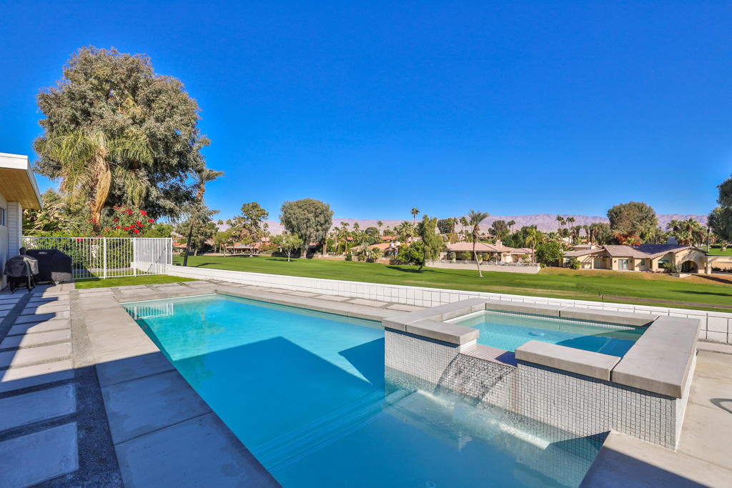 Backyard pool and raised spa with a tiled spillway, lawn, palm trees, and distant mountains.