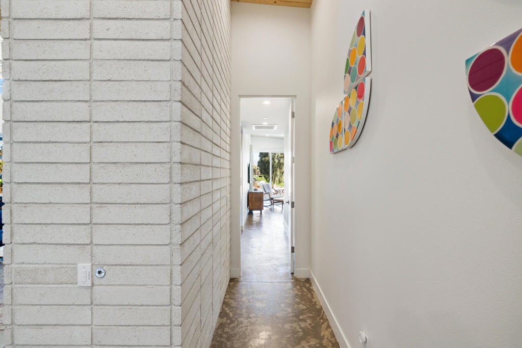 Hallway with a white block wall, polished concrete floor, and colorful circular art leading to a furnished living area.