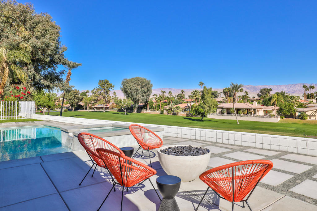 Patio with orange chairs and a fire bowl overlooking a pool, golf course, and distant mountains.