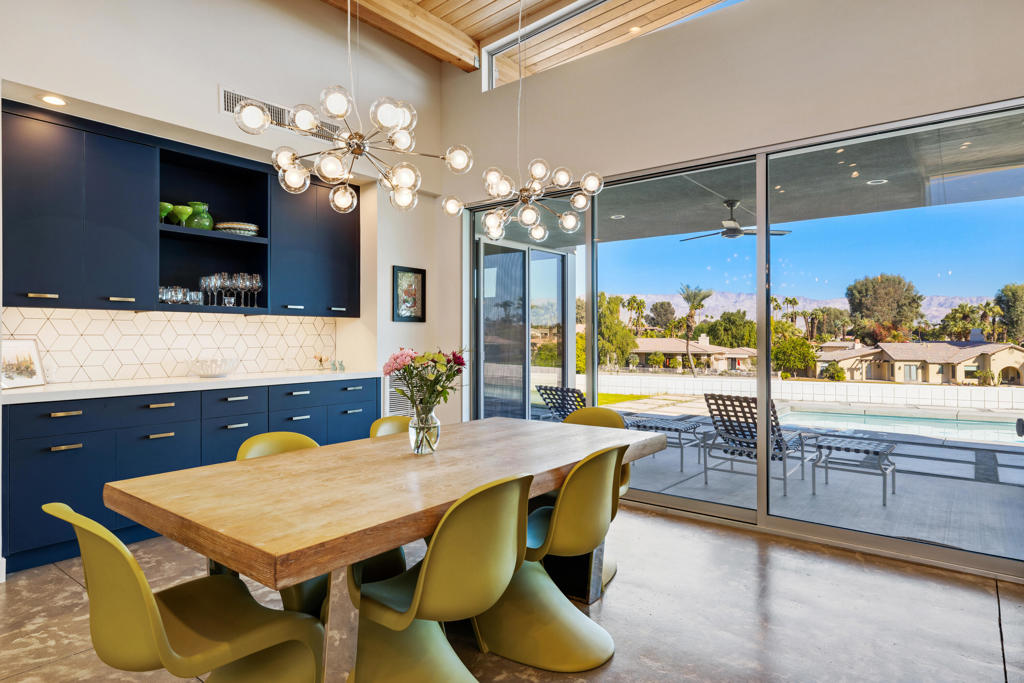 Dining area with a wood table and navy cabinets overlooking a pool and distant mountains.