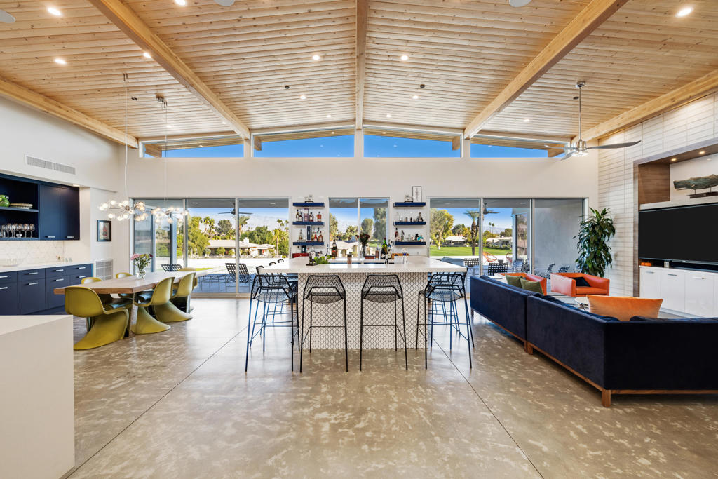 Open-plan kitchen and living area with a large island, vaulted wood ceiling, and lawn views.