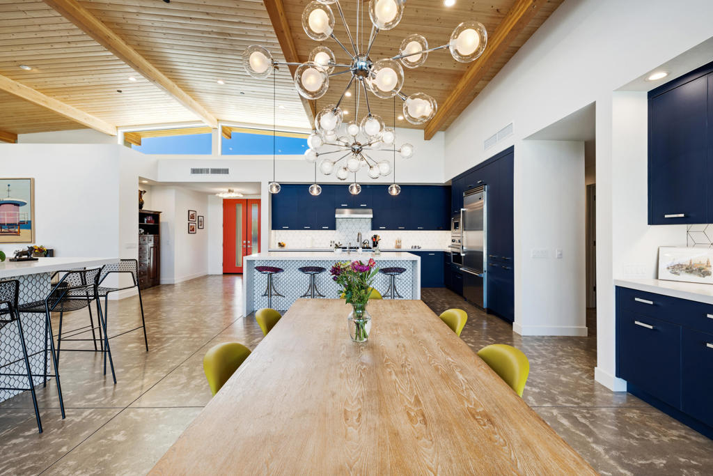 Open kitchen and dining area with navy cabinetry, a wood-beamed ceiling, and globe chandeliers.