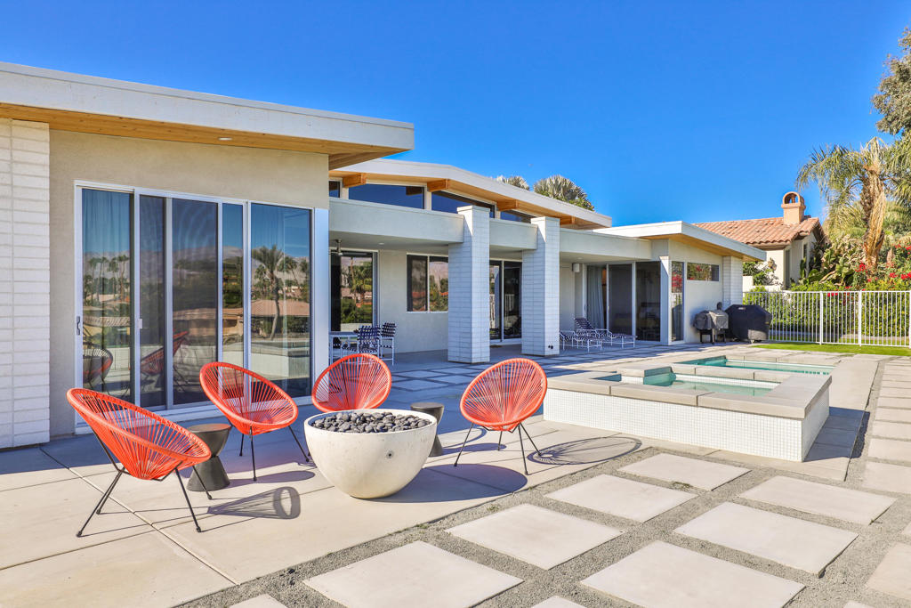 Modern home patio with a raised pool, red chairs, and a stone-filled fire bowl.