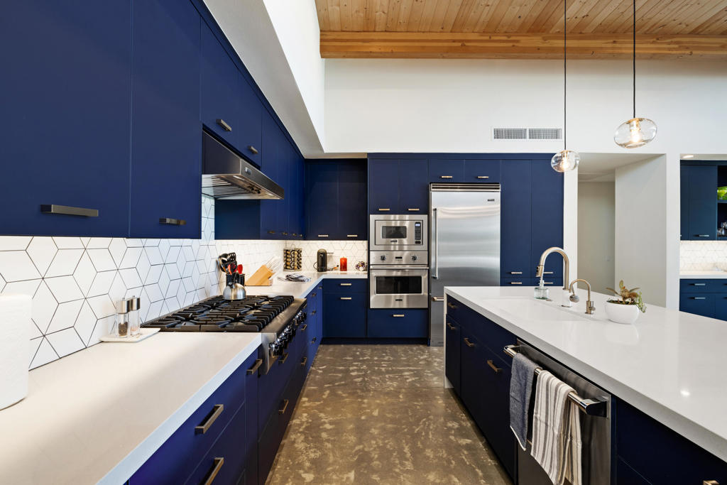Modern kitchen with blue cabinets, stainless steel appliances, and a white island beneath a wood ceiling.