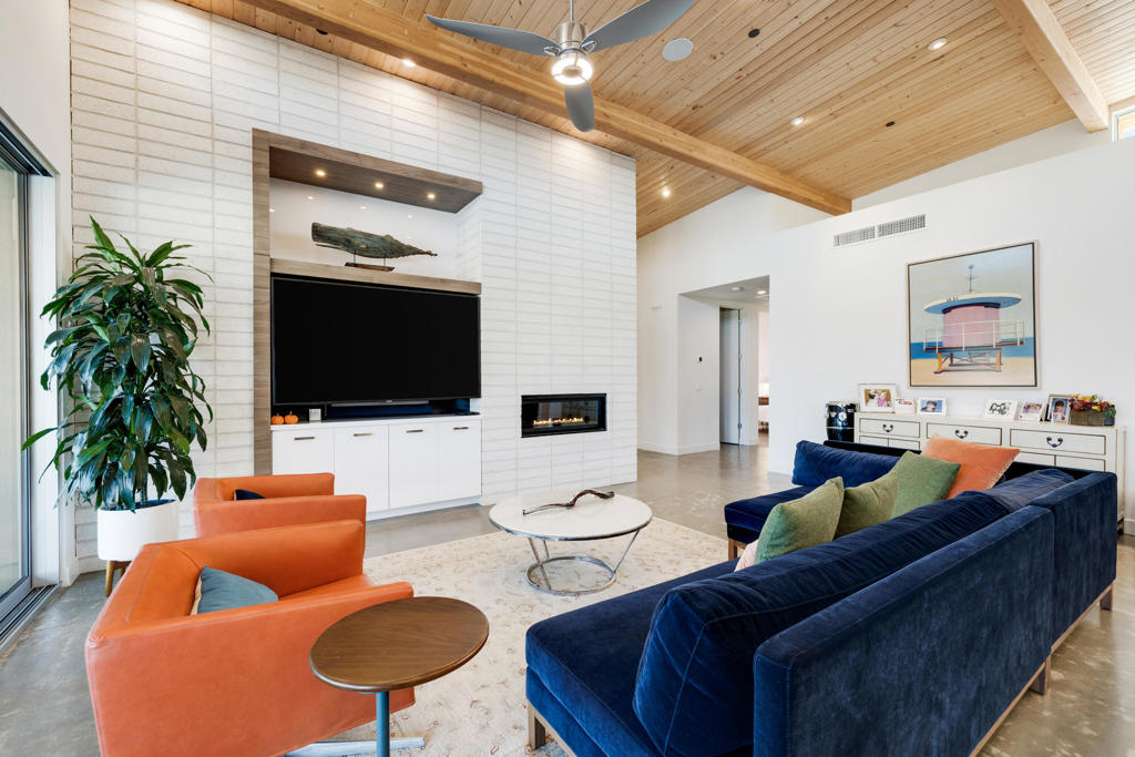 Living room with a vaulted wood ceiling, built-in television wall and fireplace, and orange and navy seating.