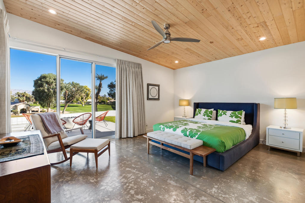 Bedroom with a wood-plank ceiling, green bedding, and sliding doors to a landscaped lawn.