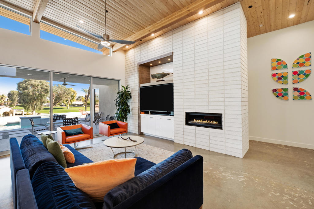Living room with a vaulted wood ceiling, tiled fireplace wall, and sliding glass doors overlooking a pool.