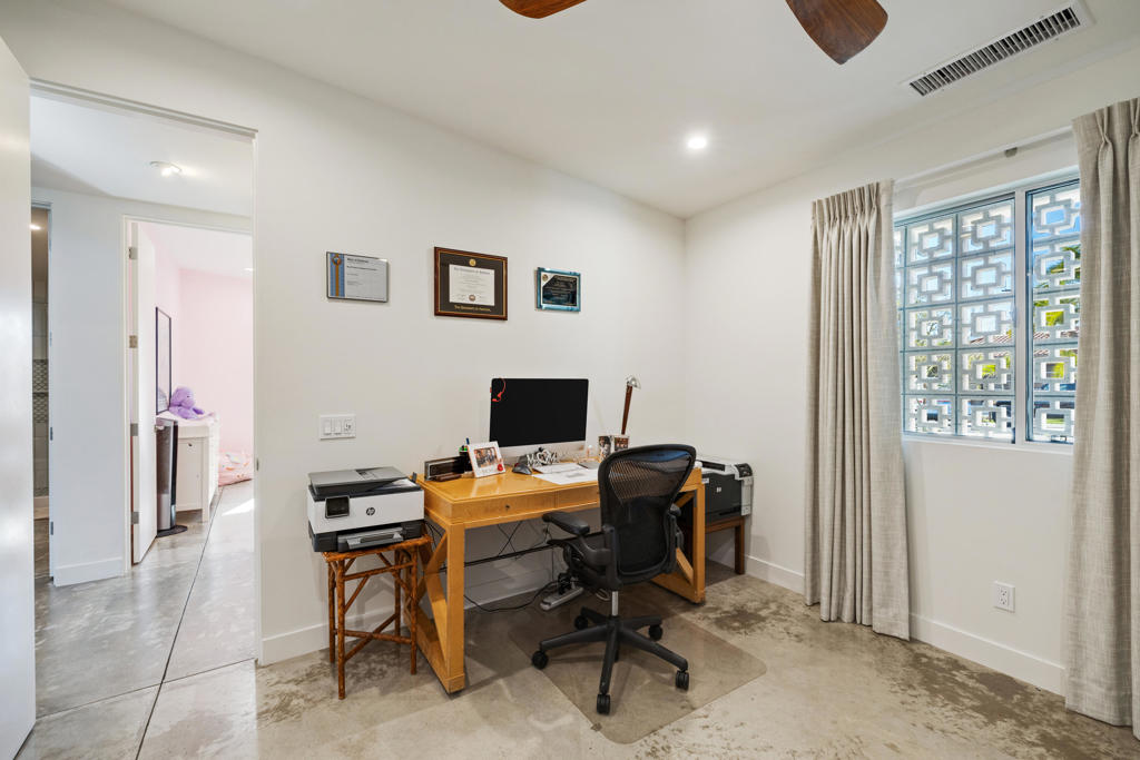 Home office with a wooden desk, computer, and chair beside a gridded window.