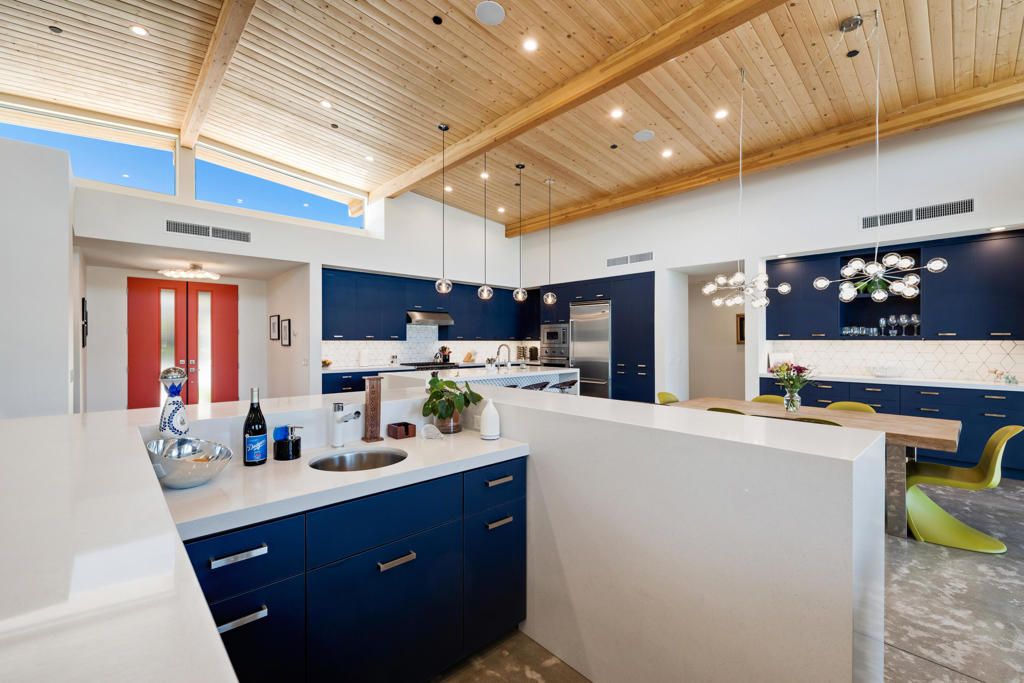 Modern kitchen with blue cabinets, a large white island, and a vaulted wood ceiling.