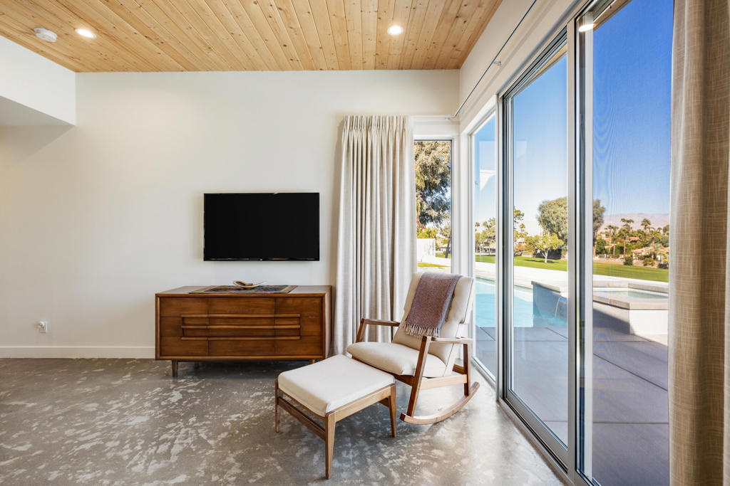 Furnished sitting area with a wood ceiling, rocking chair, and sliding doors overlooking the pool.