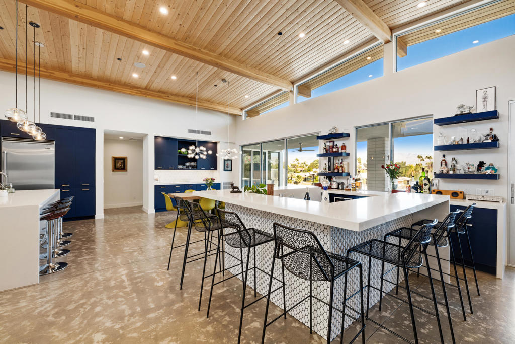 Modern kitchen with a large white island, navy cabinetry, and a vaulted wood-plank ceiling.