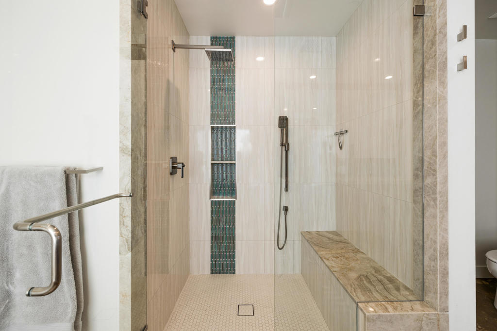 Walk-in shower with blue mosaic tile accent, handheld showerhead, and built-in stone bench.