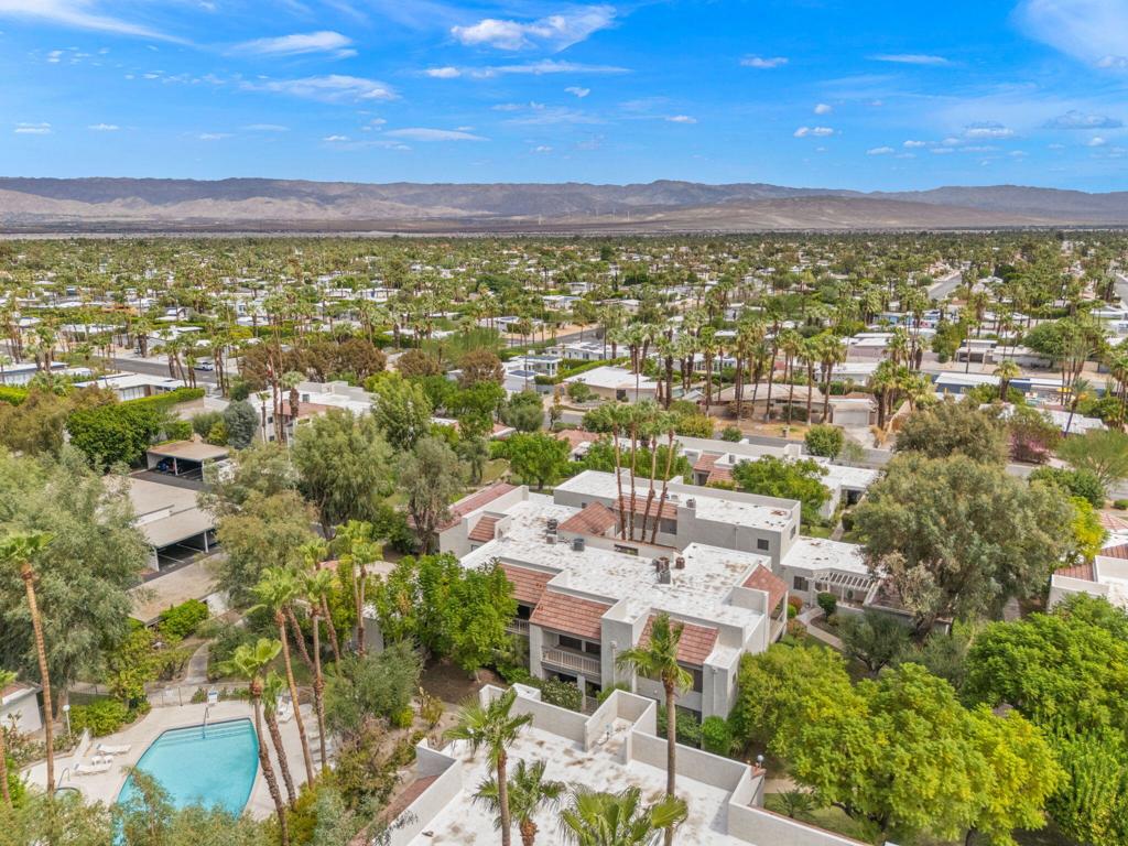 Aerial view of homes and a turquoise pool among palm trees, with mountains on the horizon.