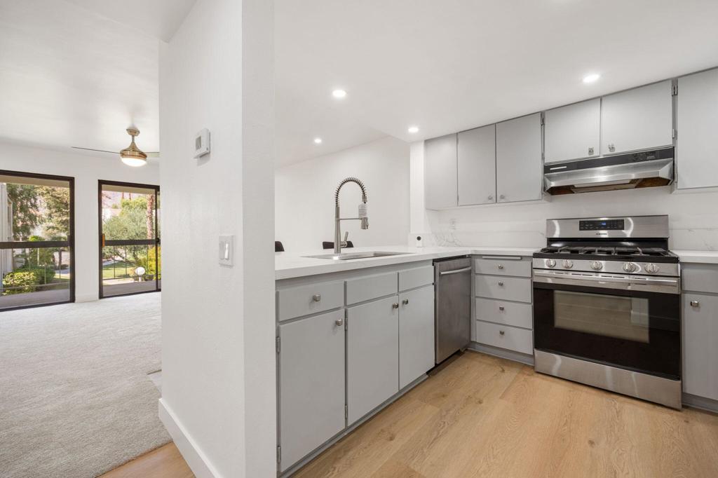 Remodeled kitchen with gray cabinets, stainless steel appliances, and light wood flooring beside sliding glass doors.