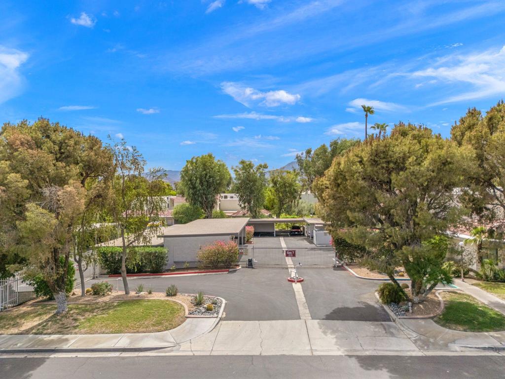 Gated residential entrance with a paved driveway, mature trees, and distant mountains.
