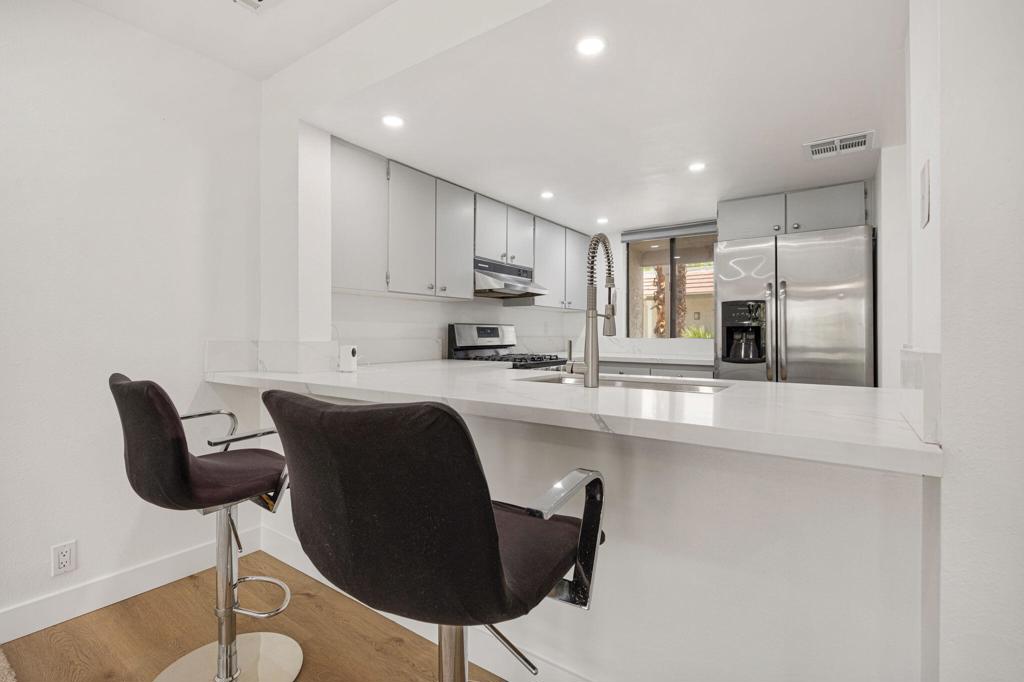 Modern white kitchen with a breakfast bar, two dark stools, and stainless steel appliances.