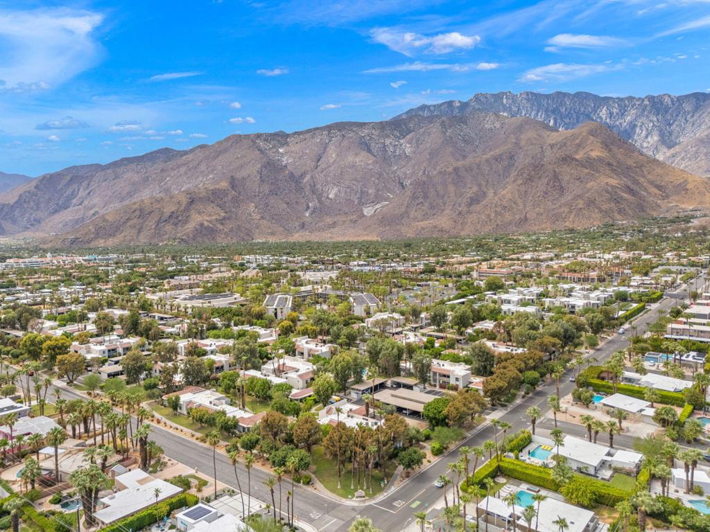 Aerial view of Palm Springs homes and palm-lined streets beneath a rugged mountain range.
