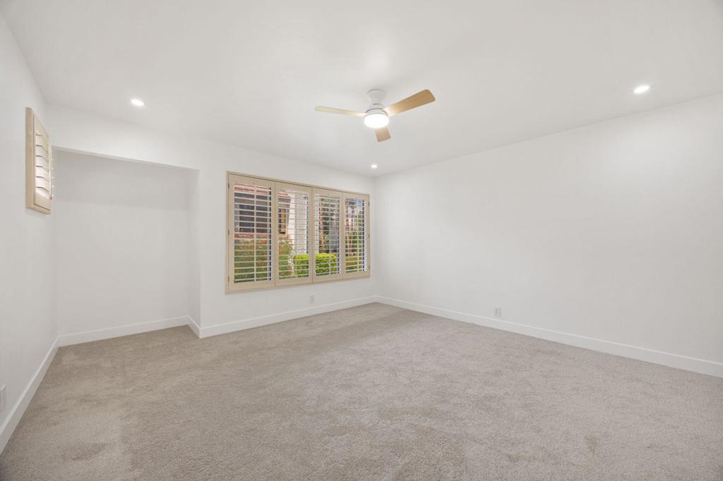 Empty carpeted bedroom with plantation-shuttered windows and a ceiling fan.