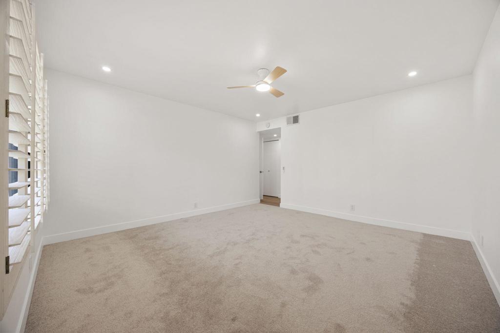 Empty carpeted bedroom with plantation shutters and a ceiling fan.