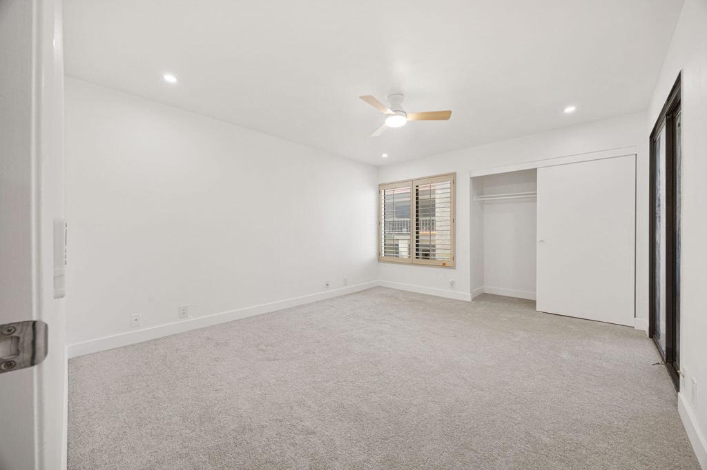 Empty carpeted bedroom with a ceiling fan, shuttered window, and open closet.