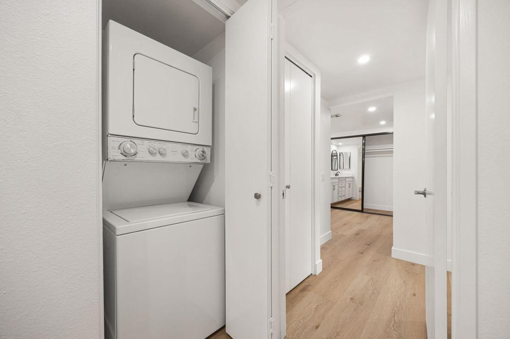 Stacked washer and dryer beside a hallway leading to a bathroom with mirrored closet doors.