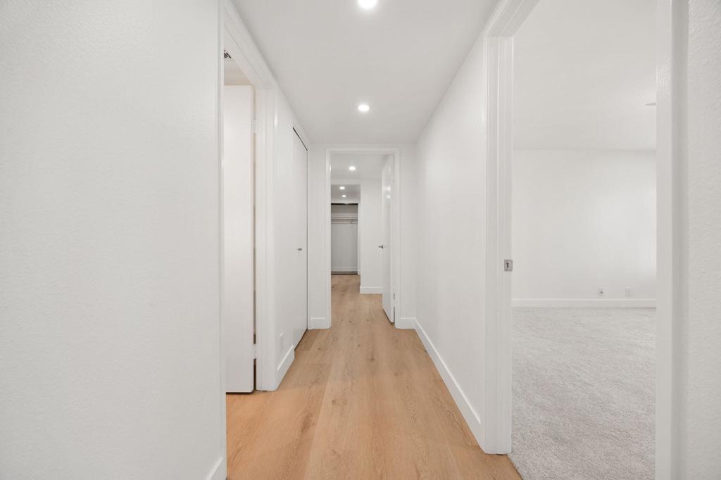 Bright hallway with light wood flooring, recessed lights, and an adjoining carpeted room.