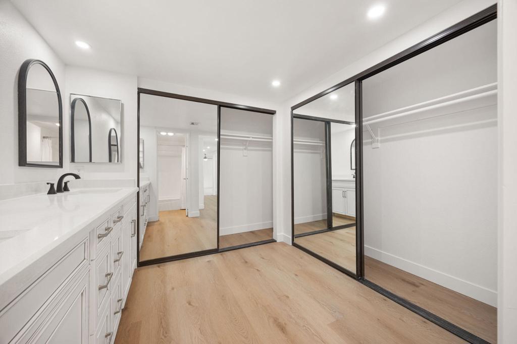 Walk-in closet with white built-in drawers, wood flooring, and large mirrored sliding doors.