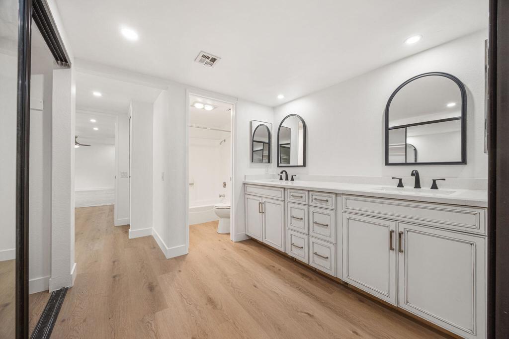 Bathroom with a long double vanity, black faucets, and three arched mirrors.