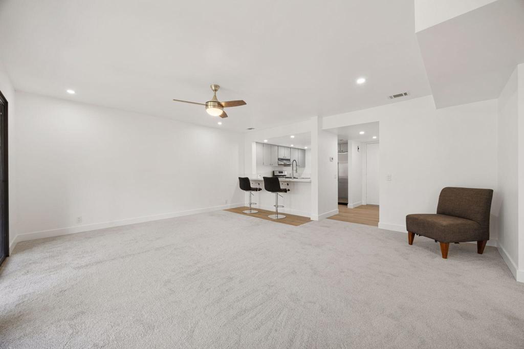 Living room with light carpeting, a ceiling fan, and an open kitchen with breakfast bar.
