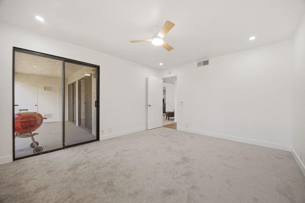 Empty carpeted room with a ceiling fan and black-framed sliding glass doors.