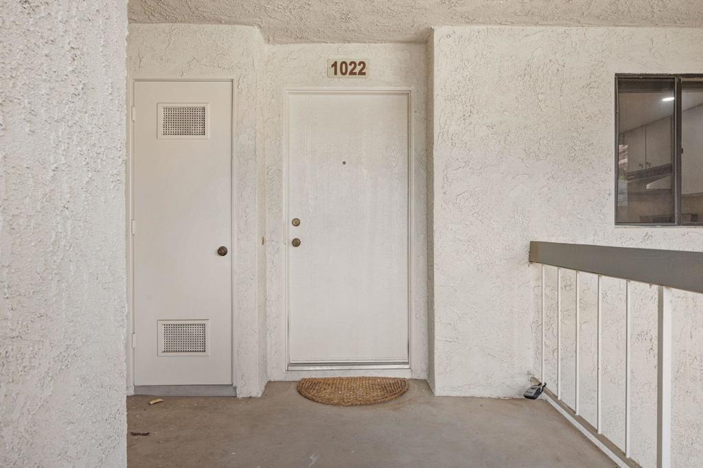Unit 1022 entrance with a white door, stucco walls, and balcony railing.