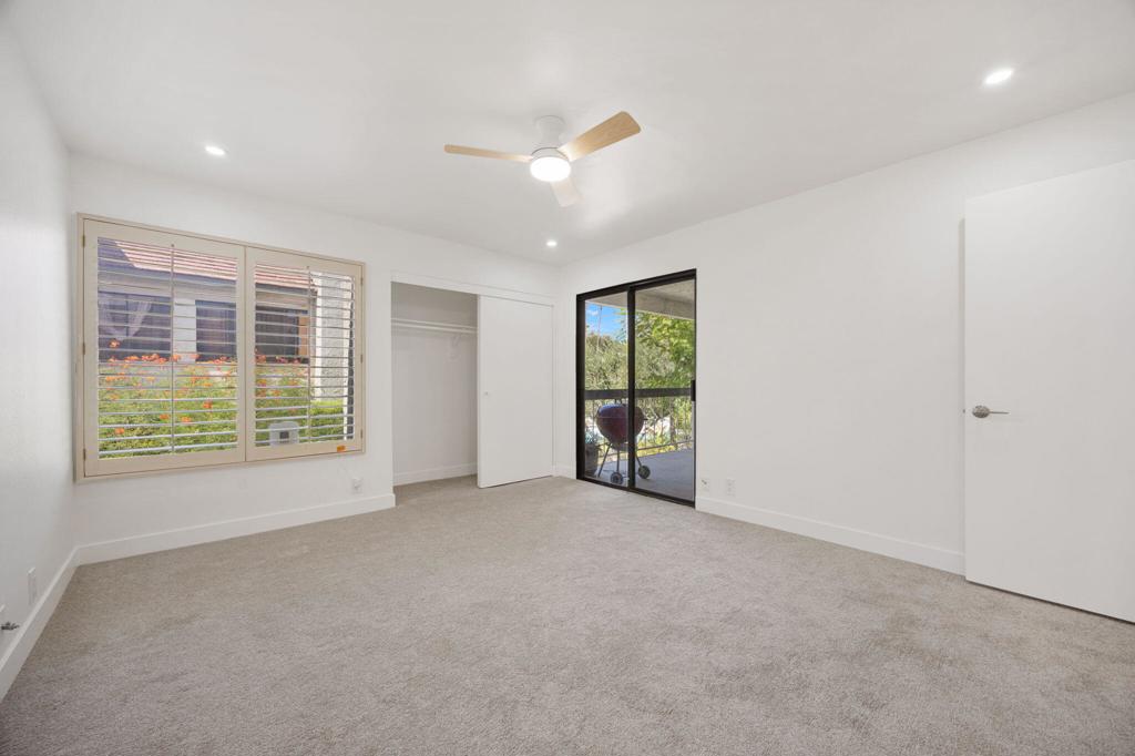 Empty carpeted bedroom with a ceiling fan, window with blinds, closet, and patio doors.