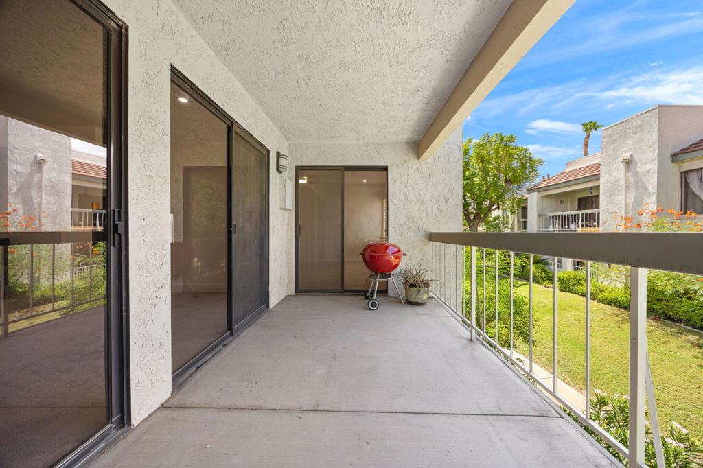 Covered balcony with sliding glass doors, a red kettle grill, and a view of the landscaped courtyard.