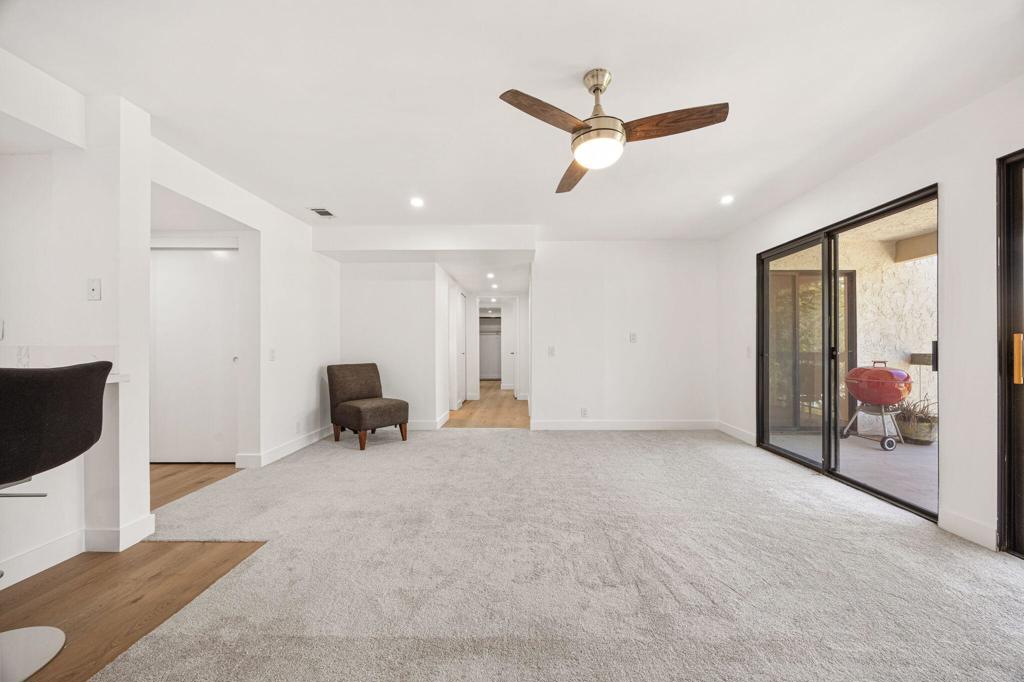 Living room with a ceiling fan, sliding patio doors, and a red grill outside.