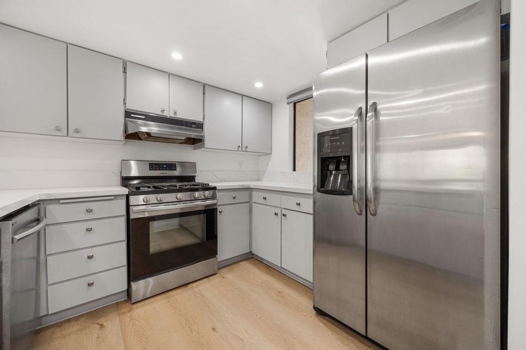 Kitchen with white cabinets, pale wood floors, and stainless steel appliances.