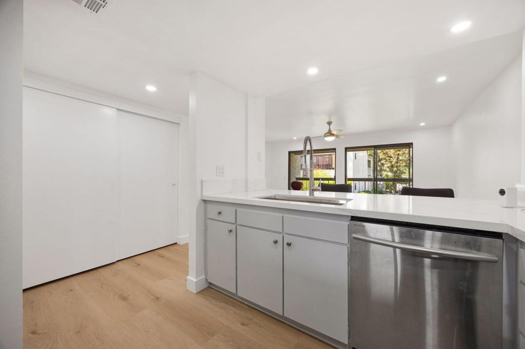Modern white kitchen with a long counter, stainless-steel dishwasher, and sliding glass doors overlooking greenery.