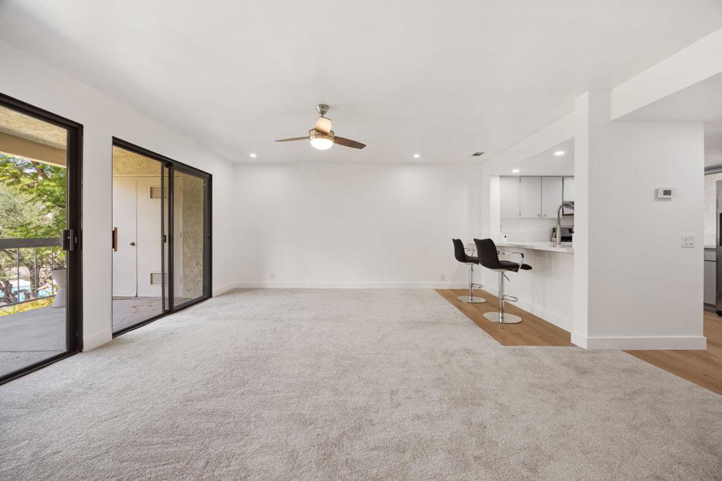 Open living room with light carpet, sliding patio doors, and a kitchen breakfast bar with two stools.
