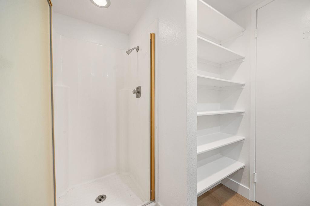 White walk-in shower beside built-in shelving with wood flooring.