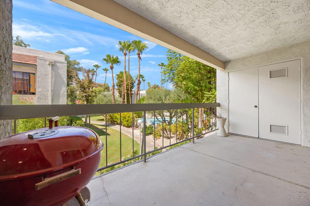 Covered balcony with a red grill overlooking palm trees and a community pool.