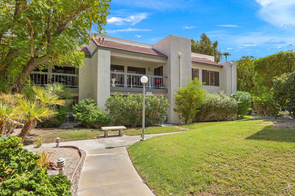 Two-story residence with balconies, landscaped shrubs, mature trees, and a curving walkway.